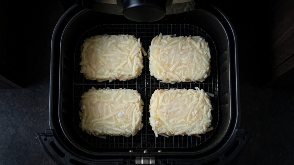Frozen hash brown patties arranged in a single layer in an air fryer basket